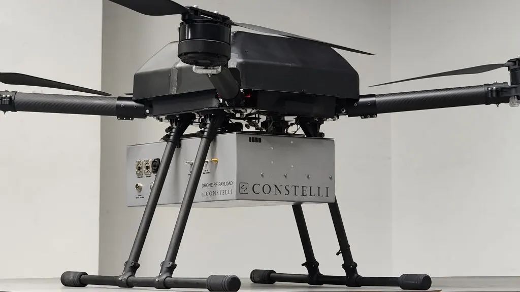 A multirotor drone carrying Constelli's branded Drone RF Payload unit beneath the airframe