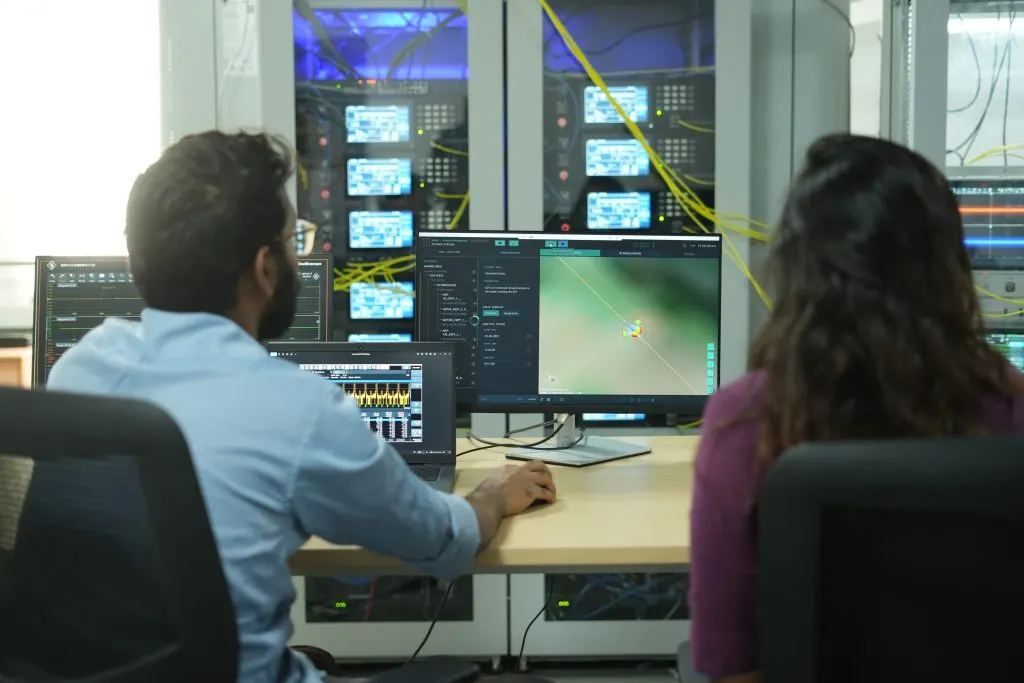 Two engineers at a Constelli electronic warfare test bench, working at operator consoles in front of a rack of instrumentation